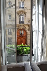 French glass windows open out to the quiet and beautiful courtyard garden below in Paris luxury apar