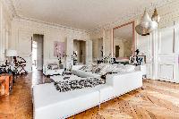 elegant living area with L-shaped sofa, chairs, wooden floor, and lamps in a 4-bedroom Paris luxury 