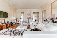 elegant living area with L-shaped sofa, chairs, wooden floor, and lamps in a 4-bedroom Paris luxury 