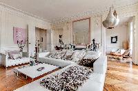 elegant living area with L-shaped sofa, chairs, wooden floor, and lamps in a 4-bedroom Paris luxury 