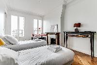 bedroom with two single beds, study desk, shelves, and ornamental fireplace in a 3-bedroom Paris lux