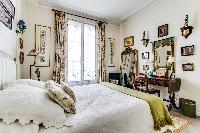 charming bedroom with a double size bed with the finest linens and a desk in a 1-bedroom Paris luxur