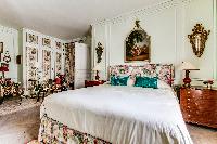 master bedroom fitted with a king size bed, armchair, round glass table, and lamp in 3-bedroom Paris