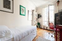 single bedroom with red study dek and chair, bookshelves and framed artworks in Paris luxury apartme