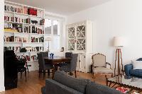 sitting room with 2 dusky sofas, white-draped windows, and a simple wooden dining table for four, we