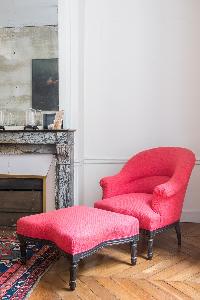 scarlet sofa chair and foot stool beside marble-tiled ornamental fireplace in Paris luxury apartment