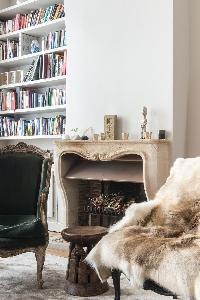 fireplace in cream palette, armchair, antique piece, and pile of books in Paris luxury apartment