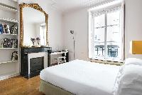 second bedroom with a queen-size bed and black ornamental fireplace beneath ornate mirror in Paris l
