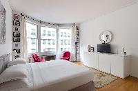 cozy master bedroom with a king-size bed and two plump pink armchairs in Paris luxury apartment