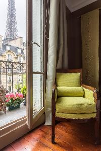 lemon-yellow armchair beside the tall window with potted flowering plants and view of Eiffel tower  