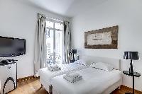 cozy bedroom with a queen-size bed, two-bed side tables, and drape curtains in paris luxury apartmen