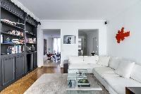 well-lit and spacious living area with two white sofas, black built-in bookshelf filled with books, 