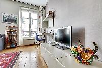 living area with a television, a music player, a desk beside the bright window, and a wooden floor i