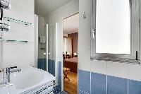 blue-tiled bathroom furnished with a shower area, a sink, a mirror, and a hairdryer with access to t
