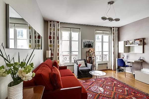 living room with a desk beside the bright windows, and red sofa bed in paris luxury apartment