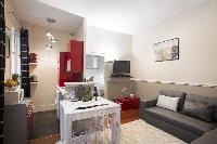 open-plan living area with a gray sofa bed, gray and white cushions, a TV, stylish lamps, white dini