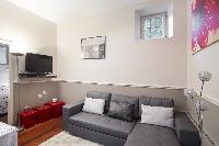 open-plan living area with a gray sofa bed, gray and white cushions, a TV, stylish lamps, white dini