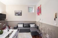 open-plan living area with a gray sofa bed, gray and white cushions, a TV, stylish lamps, white dini