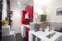 equipped kitchen in red and white hues and white dining table in a 1-bedroom Paris luxury apartment 