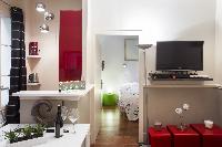 open-plan living area with a gray sofa bed, gray and white cushions, a TV, stylish lamps, white dini