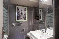 modern bathroom with gray tiles, a bathtub with integrated shower, and a toilet in a Paris luxury ap