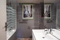modern bathroom with gray tiles, a bathtub with integrated shower, and a toilet in a Paris luxury ap