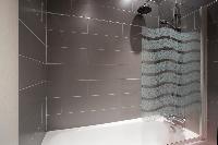 modern bathroom with gray tiles, a bathtub with integrated shower, and a toilet in a Paris luxury ap