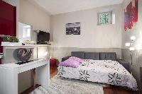 open-plan living area with a gray sofa bed, gray and white cushions, and a TV,in a Paris luxury apar