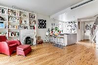 fully equipped open kitchen and living area with red chair, bookshelves, and fireplace in a Paris lu