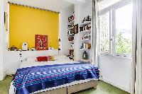 first bedroom with queen size bed, bright yellow wall, and book shelves in a Paris luxury apartment