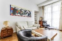 spacious living area with double-glazed windows, sofa, armchairs, paintings, shelves, nightstand, an