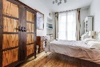 first bedroom with a queen size bed, rustic cabinet, shelves, nightstand, and lamp in a 2-bedroom Pa