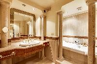 an elegant marble en-suite bathroom with a bathtub, a detachable shower head, a sink, a mirror, and 