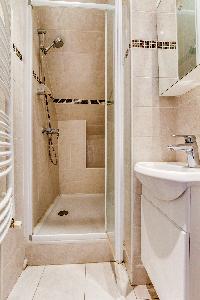 white and beige-tiled bathroom with shower and sink in a 2-bederoom Paris apartment