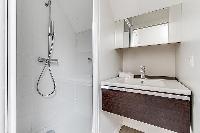 bathroom with a toilet, a sink, a mirror, and shower area in a 2-bedroom Paris luxury apartment