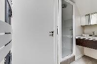 bathroom with a toilet, a sink, a mirror, and shower area in a 2-bedroom Paris luxury apartment