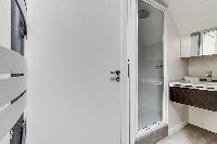 bathroom with a toilet, a sink, a mirror, and shower area in a 2-bedroom Paris luxury apartment
