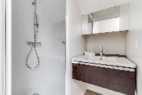 bathroom with a toilet, a sink, a mirror, and shower area in a 2-bedroom Paris luxury apartment
