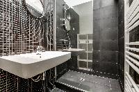 sleek gray-tiled bathroom with a sink, mirror, toilet, and shower area  in Paris luxury apartment