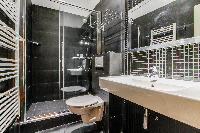 second bathroom with a large sink, a mirror, a toilet, and shower area in Paris luxury apartment