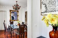 elegant dining area with a long table, six chairs, and paintings in a 3-bedroom Paris luxury apartme