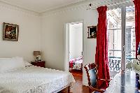 cozy master bedroom with a queen-size bed, a red drape curtain, a study desk with a chair and a lamp