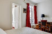 cozy master bedroom with a queen-size bed, a red drape curtain, a study desk with a chair and a lamp