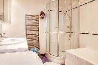 bathroom  with a toilet, a shower area, a sink, a mirror, and a full bathtub  in a 3-bedroom Paris l