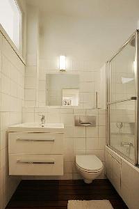 An en-suite bathroom with a toilet, a sink, a mirror, built-in cabinets, and a shower area in a 1-be
