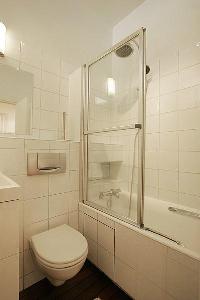 An en-suite bathroom with a toilet, a sink, a mirror, built-in cabinets, and a shower area in a 1-be