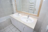 white bathroom with built-in cabinet, double sinks, toilet, and bathtub in a 2-bedroom Paris luxury 