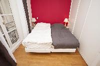 second bedroom with two single beds, two bedside tables with lamps, and a French window with courtya