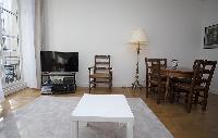 cozy living area with a center table, a chair, a TV and a lamp in a 2-bedroom Paris luxury apartment
