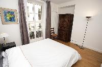 master bedroom with a queen-size bed, two bedside tables with lamps, a chair, a cabinet, and a Frenc